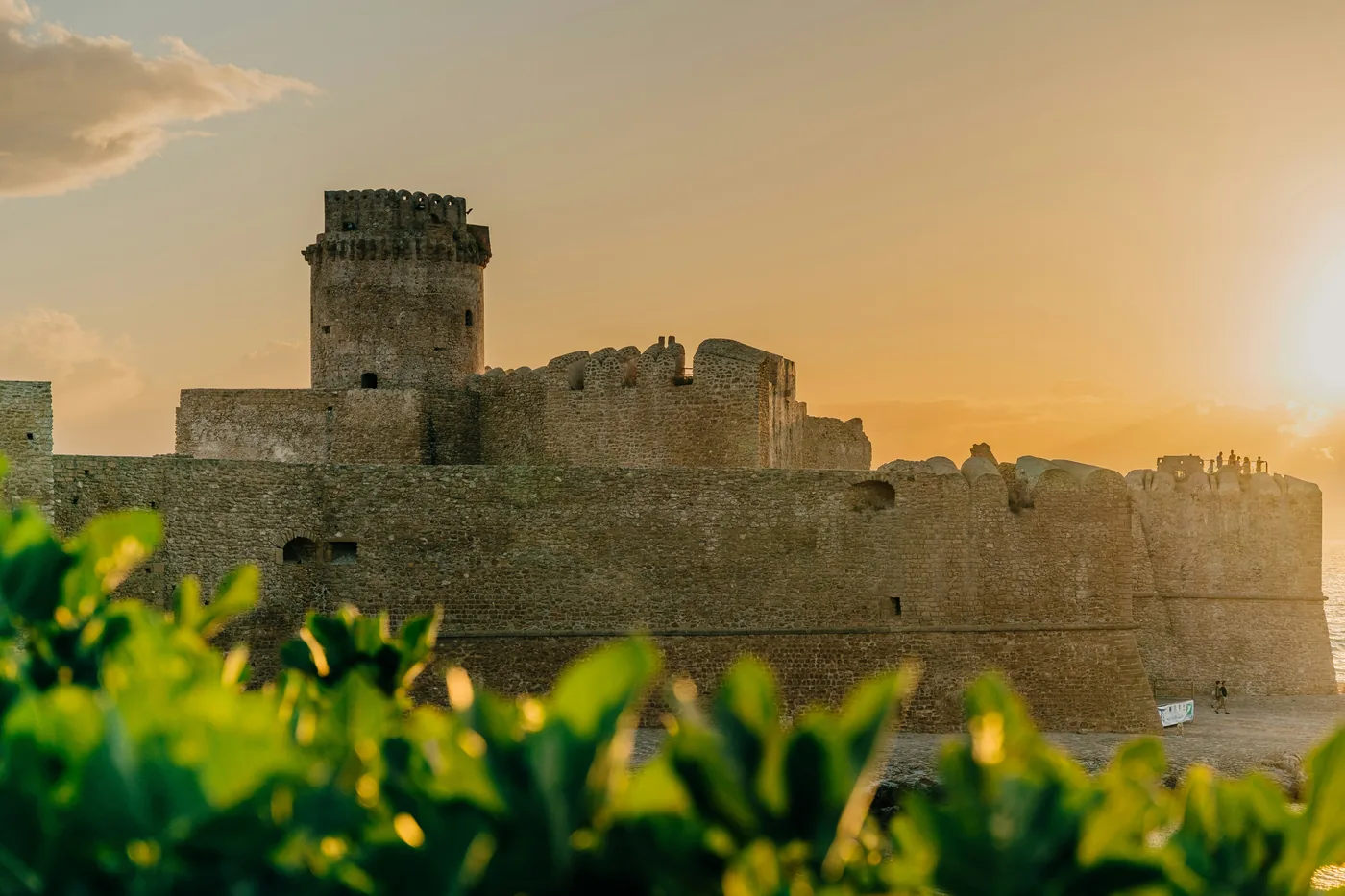 Il castello aragonese di Le Castella nella luce calda del tramonto, oltre una siepe verde