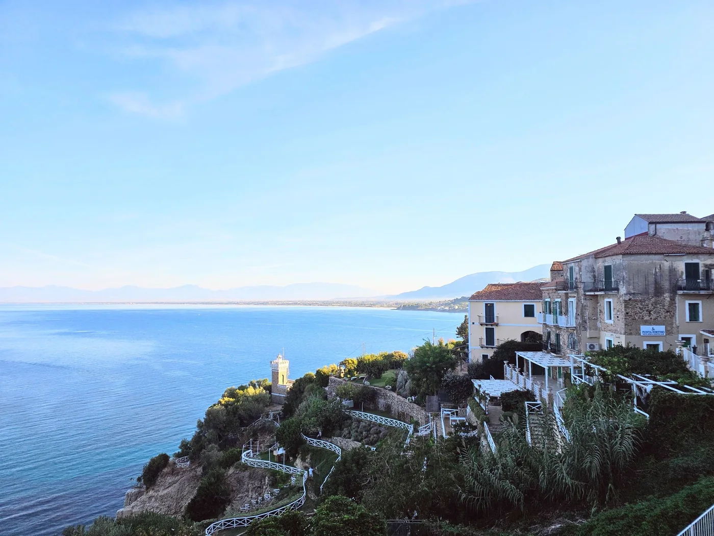 Il golfo di Salerno visto dall'alto da Agropoli, con una piccola torre-faro fra i giardini a terrazze sulla scogliera e le montagne in fondo.