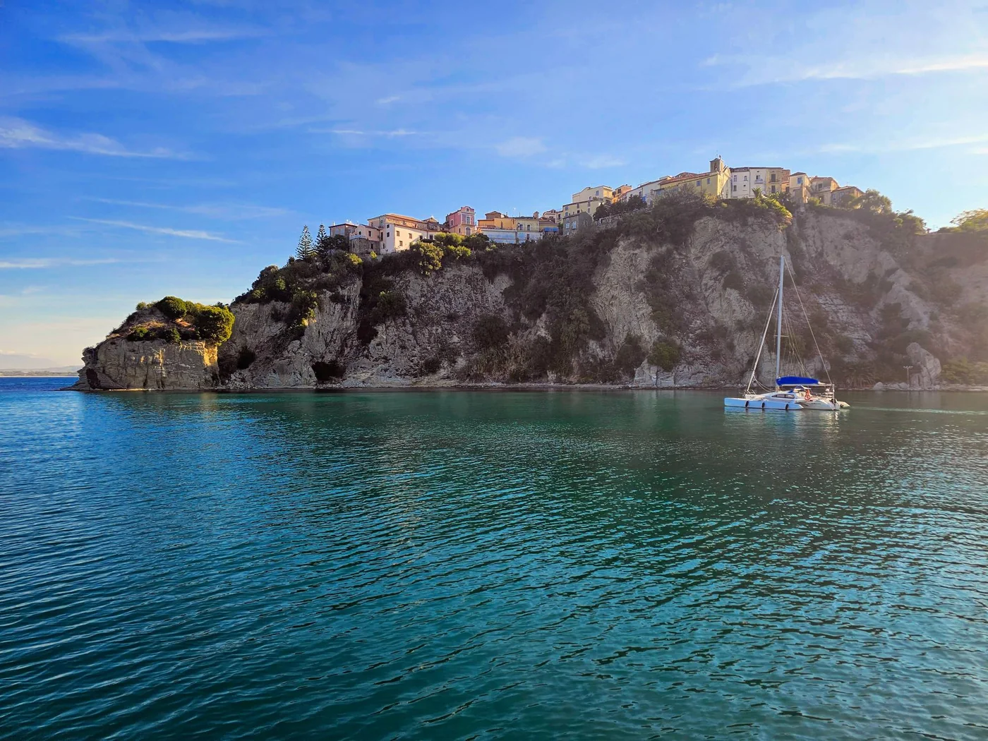 Il centro storico di Agropoli arroccato sulla scogliera sopra il mare turchese, con un catamarano alla fonda nella baia.