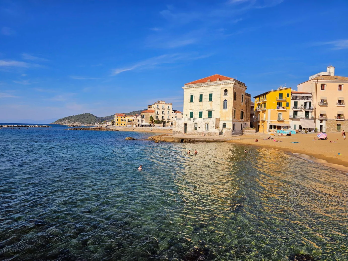 L'acqua limpida del mare di Santa Maria di Castellabate, con la spiaggia, il palazzo color crema e le case gialle.