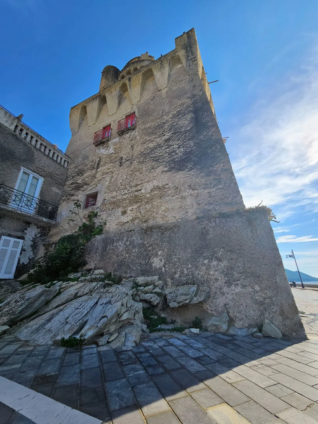 La torre di pietra di Santa Maria di Castellabate vista dal basso, con le finestre dalle inferriate rosse e il cielo blu.