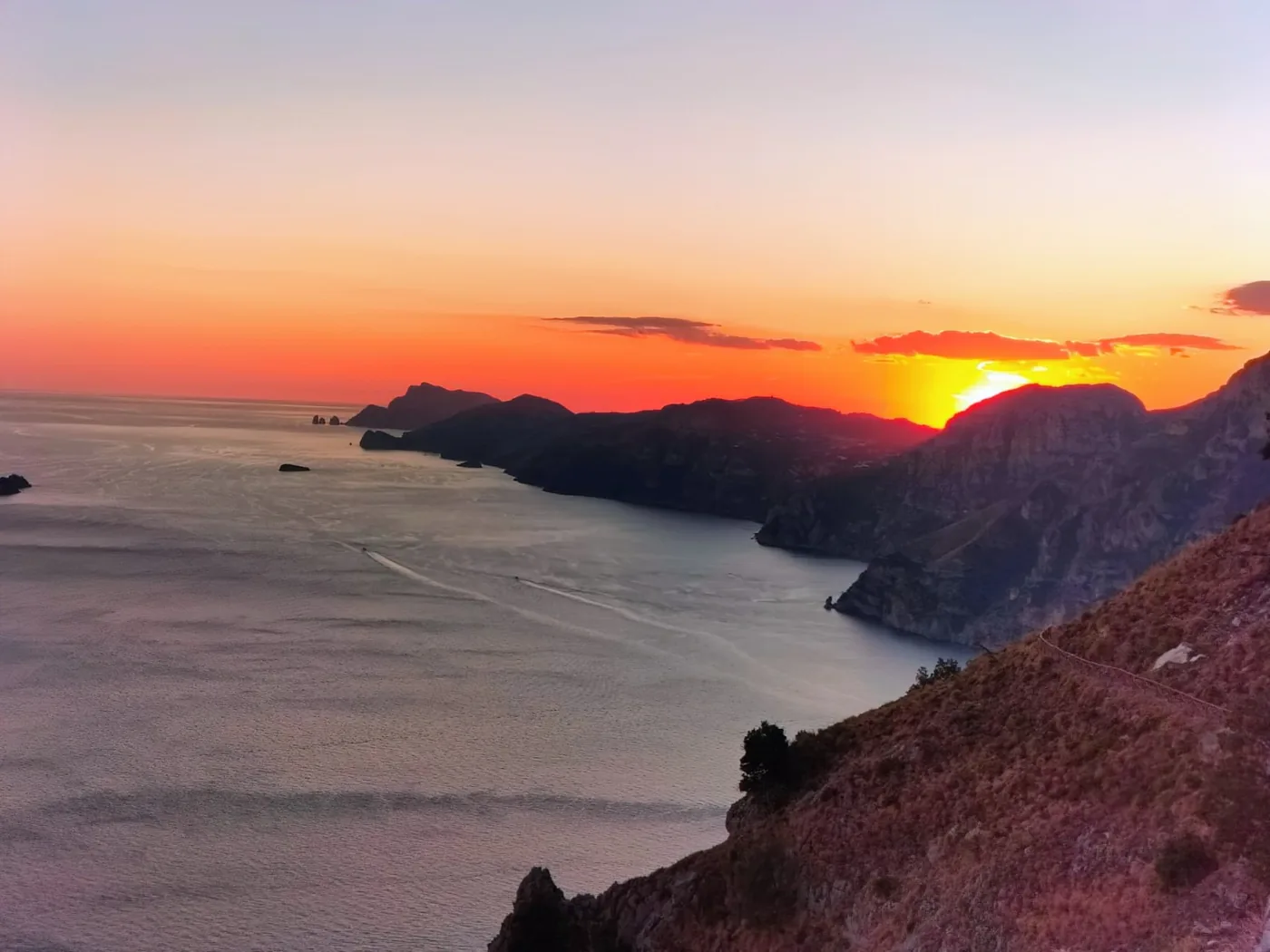 Il sole che tramonta dietro i promontori della costiera amalfitana, sopra un mare dorato