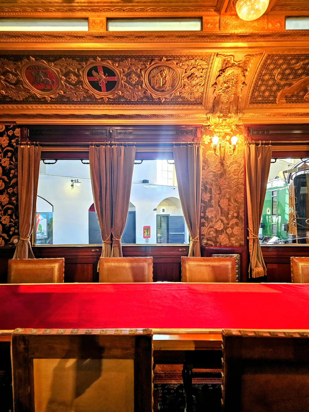 L'interno di una carrozza salone d'epoca, con i pannelli di legno intagliato, le tende e un lungo tavolo rosso
