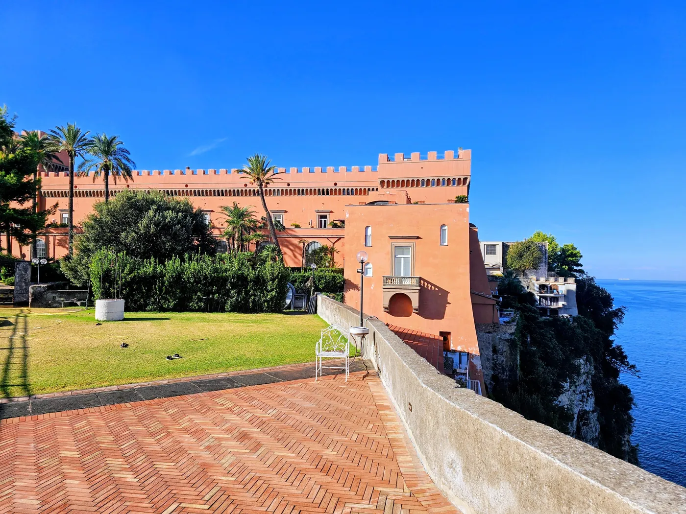 La terrazza di cotto con le palme del Castello Giusso e la sua ala rossa merlata sul bordo della scogliera