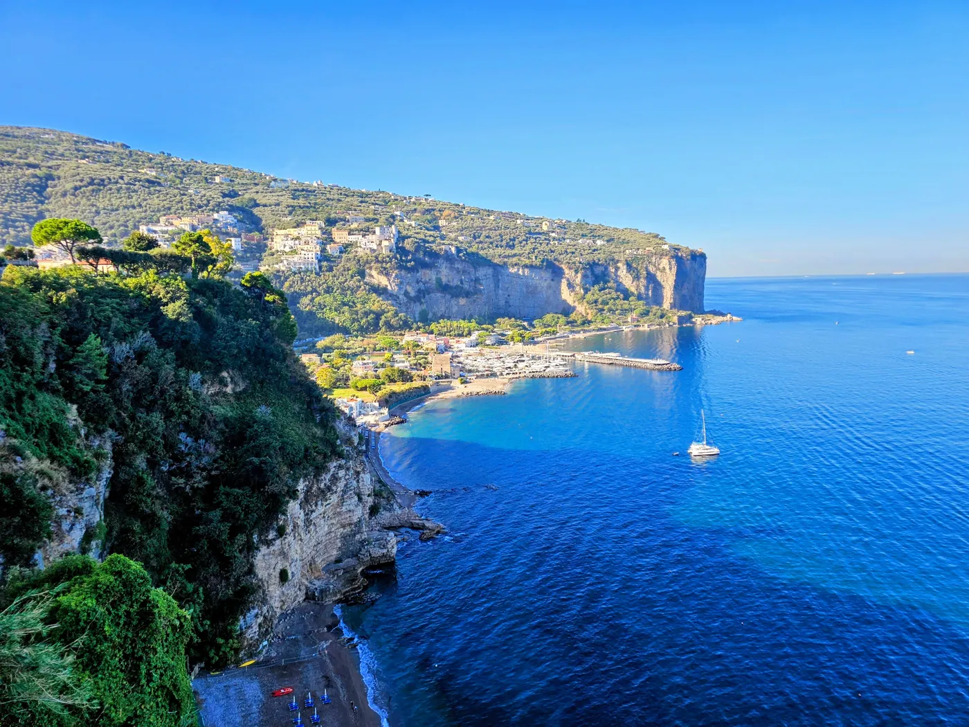La costa a picco della penisola sorrentina, con una baia e una barca a vela sul mare blu