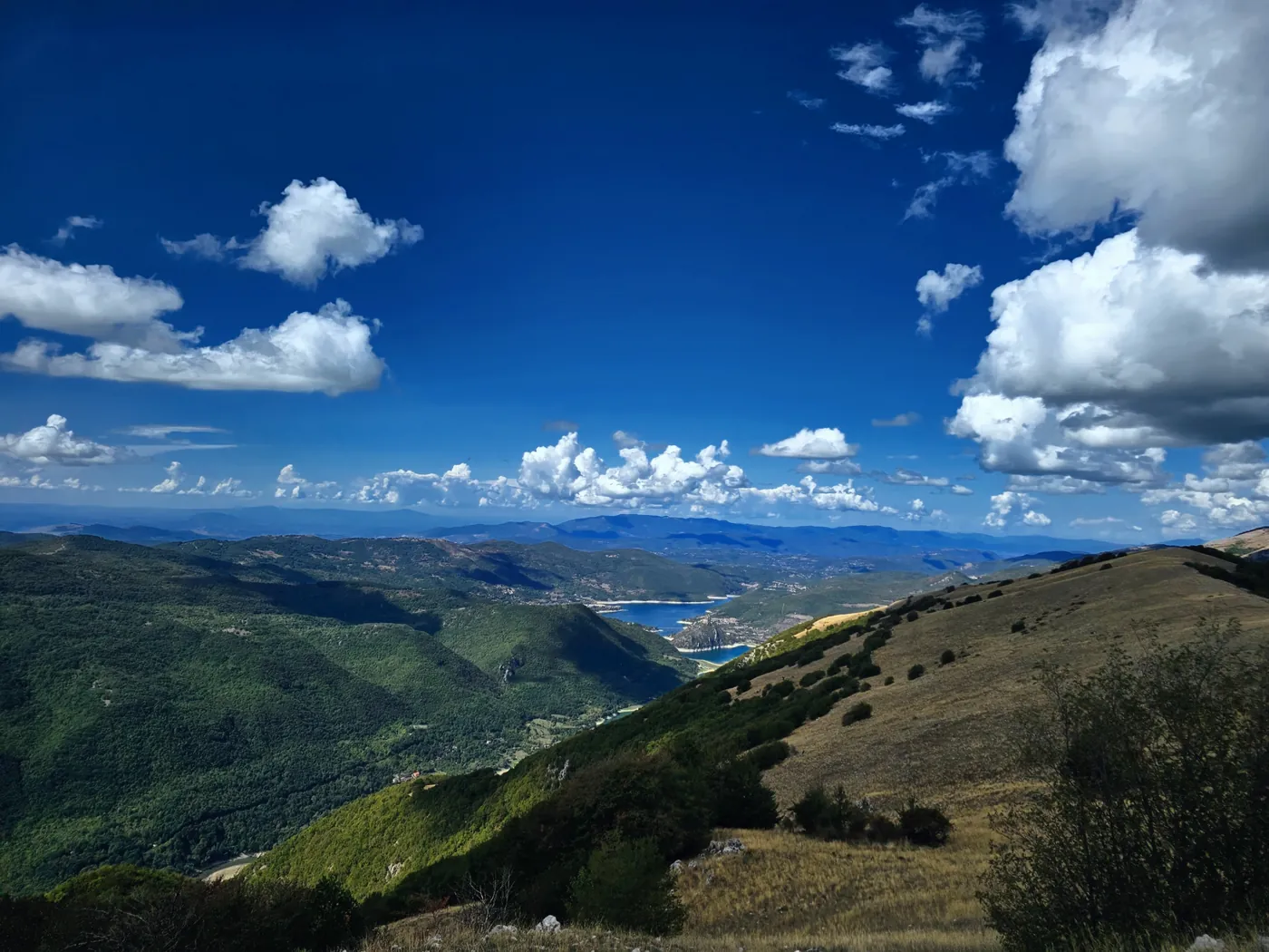 Crinali verdi e, in fondo alla valle, il lago del Turano sotto un cielo blu pieno di nuvole