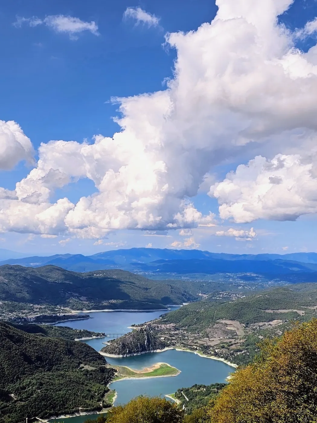 Il lago del Turano visto dall'alto, con le sue anse tra i monti boscosi sotto grandi nuvole bianche