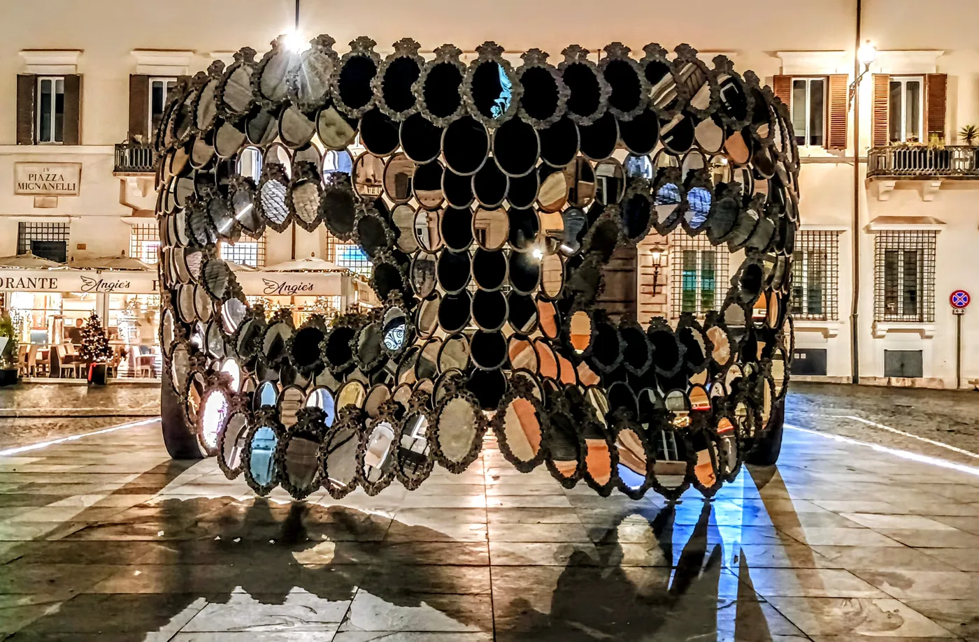 Una grande installazione fatta di specchi ovali in piazza Mignanelli, di sera, tra le vetrine illuminate