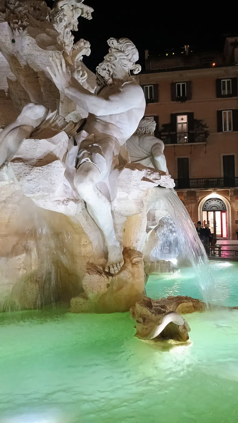 Le statue di marmo della fontana dei Quattro Fiumi a piazza Navona, illuminate di notte, sopra l'acqua verde della vasca