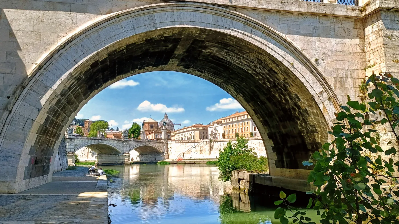 L'arcata di un ponte sul Tevere incornicia il fiume, un altro ponte e una cupola sullo sfondo