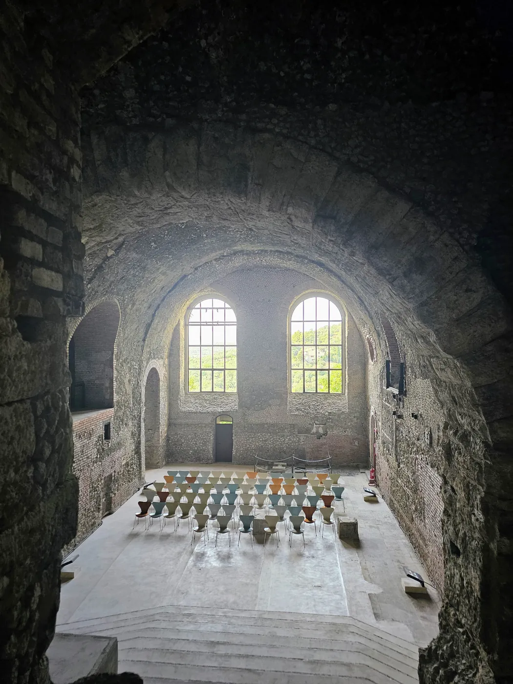 Una grande sala voltata del santuario di Ercole Vincitore a Tivoli, con due finestroni e file di sedie colorate